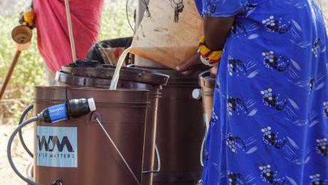 During a water purification demonstration, a woman pours contaminated water into a bucket equipped with water filters.
